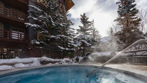 Un bain à remous entouré d’arbres couverts de neige et d’un bâtiment en bois.