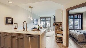 Una cocina moderna con una isla central, un comedor con un muro de acento de piedra y un dormitorio con un gran ventanal.