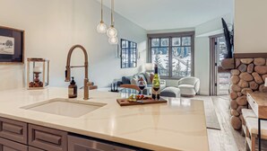 Une cuisine moderne dotée d’un grand îlot central, d’une cheminée en pierre et offrant une vue sur un paysage enneigé par les fenêtres.
