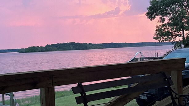 A wooden deck with a bench overlooking a body of water, a dock, and a vehicle. - Lake front hideaway with spectacular views. (Hemphill)