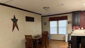 A dining area with a wooden table and chairs, a kitchen with a bar area, and a window with blinds. - Lake front hideaway with spectacular views. (Hemphill)