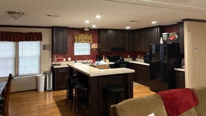 A compact kitchen with dark wooden cabinets, a central island with stools, a refrigerator, and a coffee maker. - Lake front hideaway with spectacular views. (Hemphill)