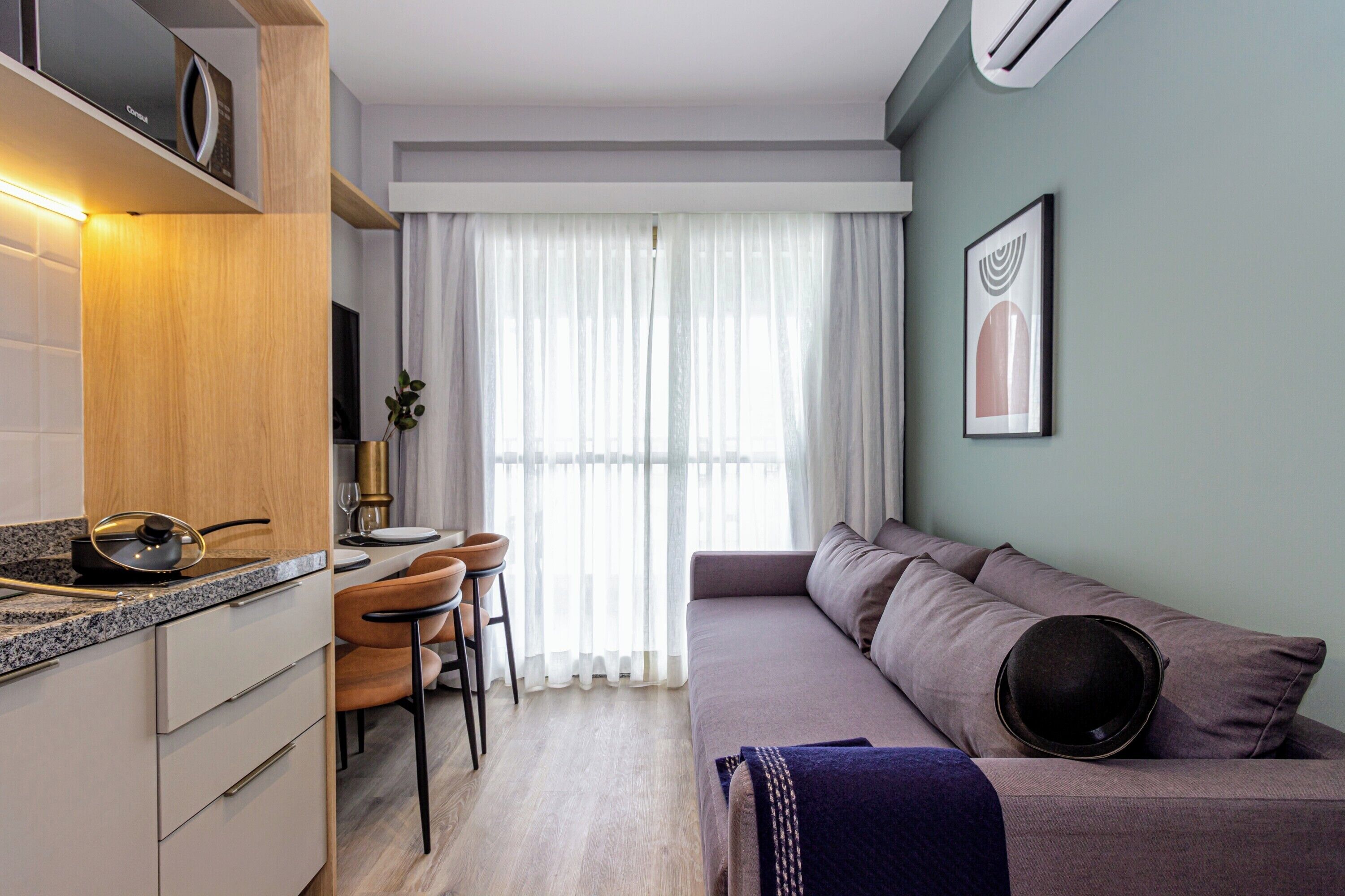 A modern kitchen with a dining area, a sofa, and a large window with sheer curtains.