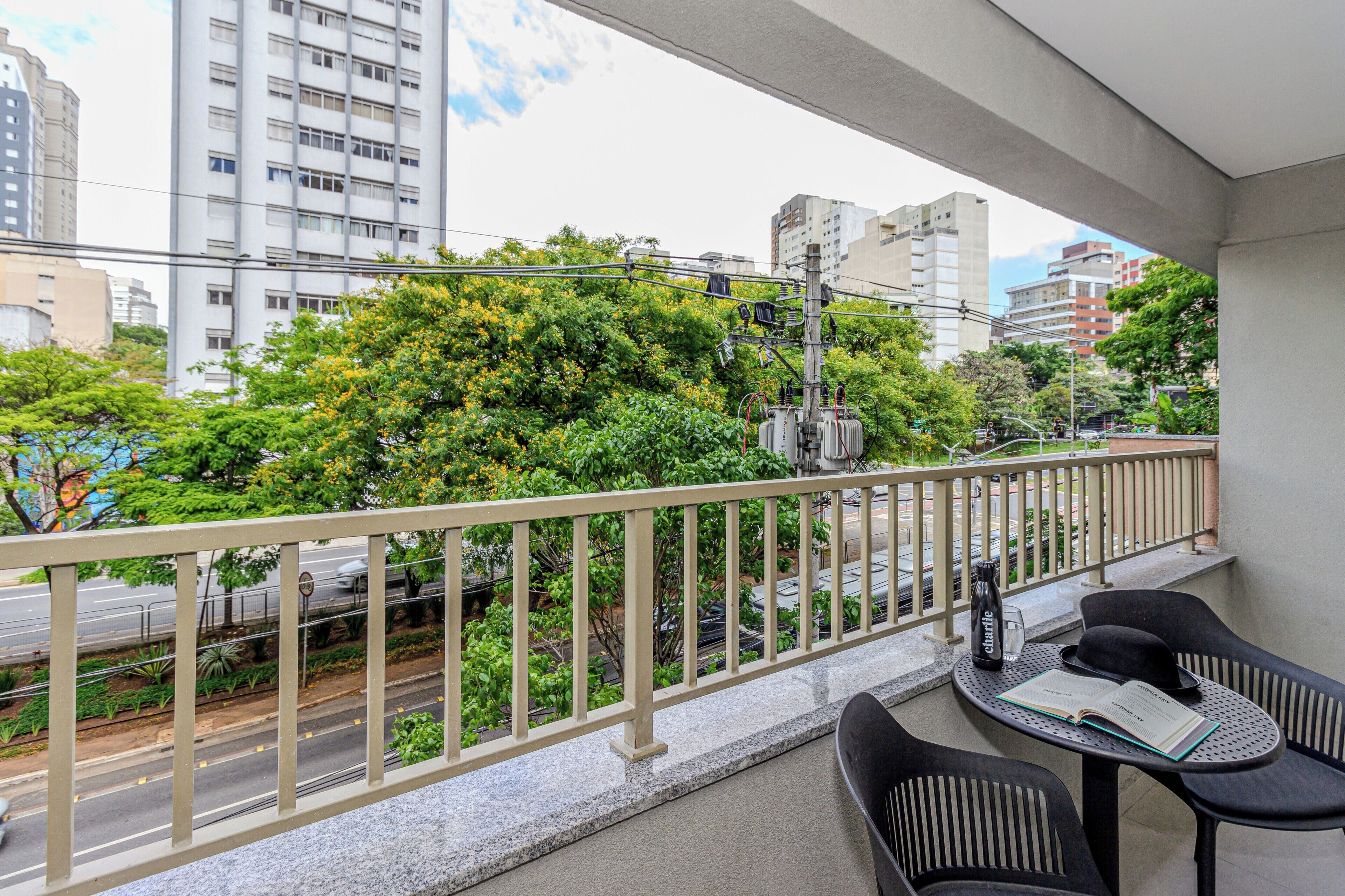 Un balcon avec une table, des chaises, un livre et une bouteille.