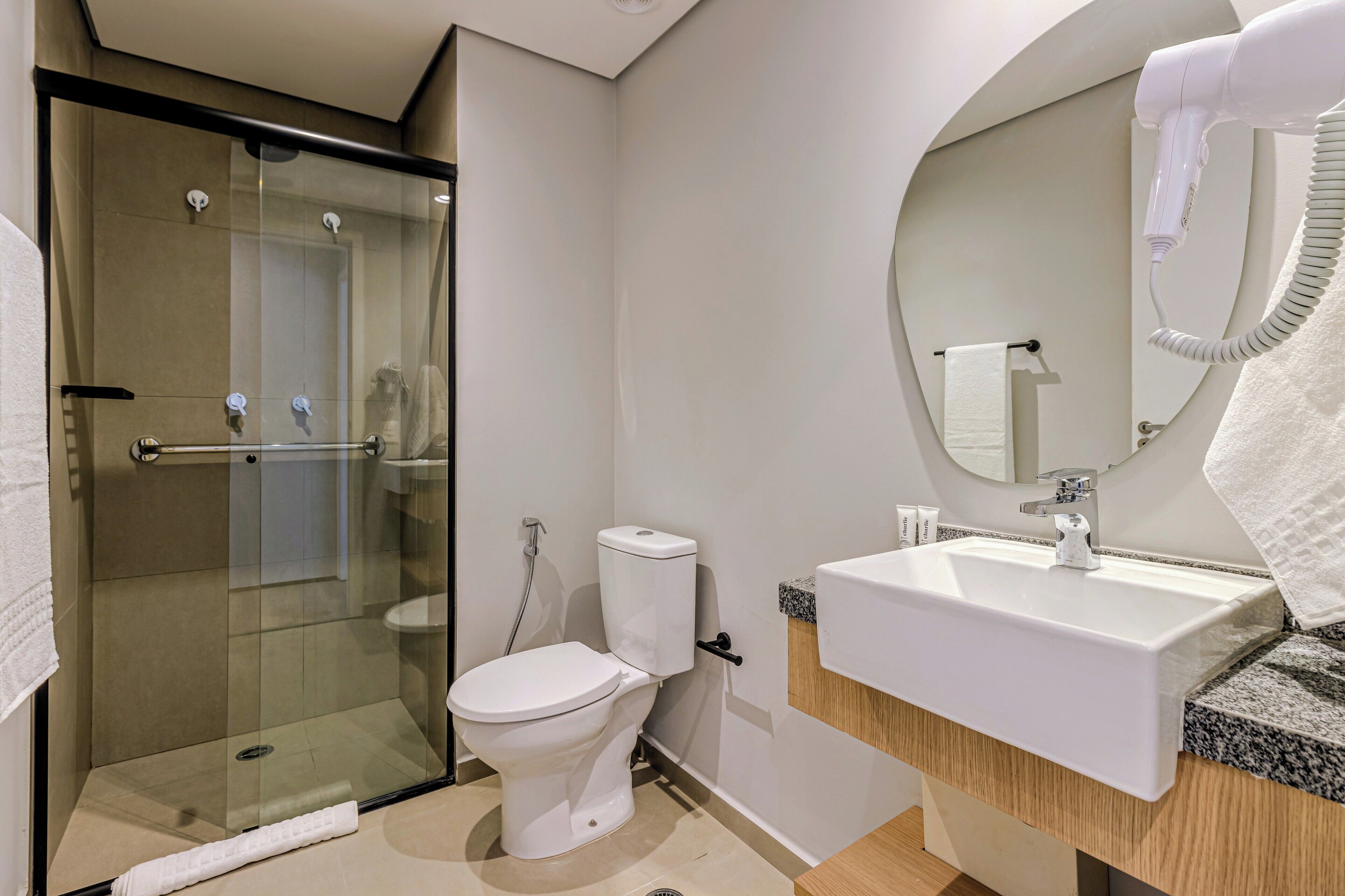 A modern bathroom with a glass-enclosed shower, a white toilet, a sink with a mirror, and a hairdryer on the wall.