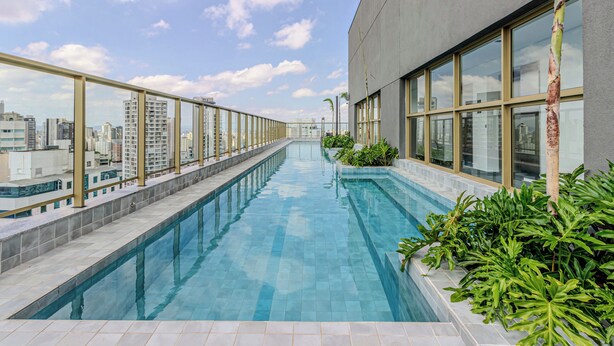 A rooftop swimming pool with a city view, surrounded by glass railings and plants. - Charlie Nik Paradiso \ Soft Opening (São Paulo)