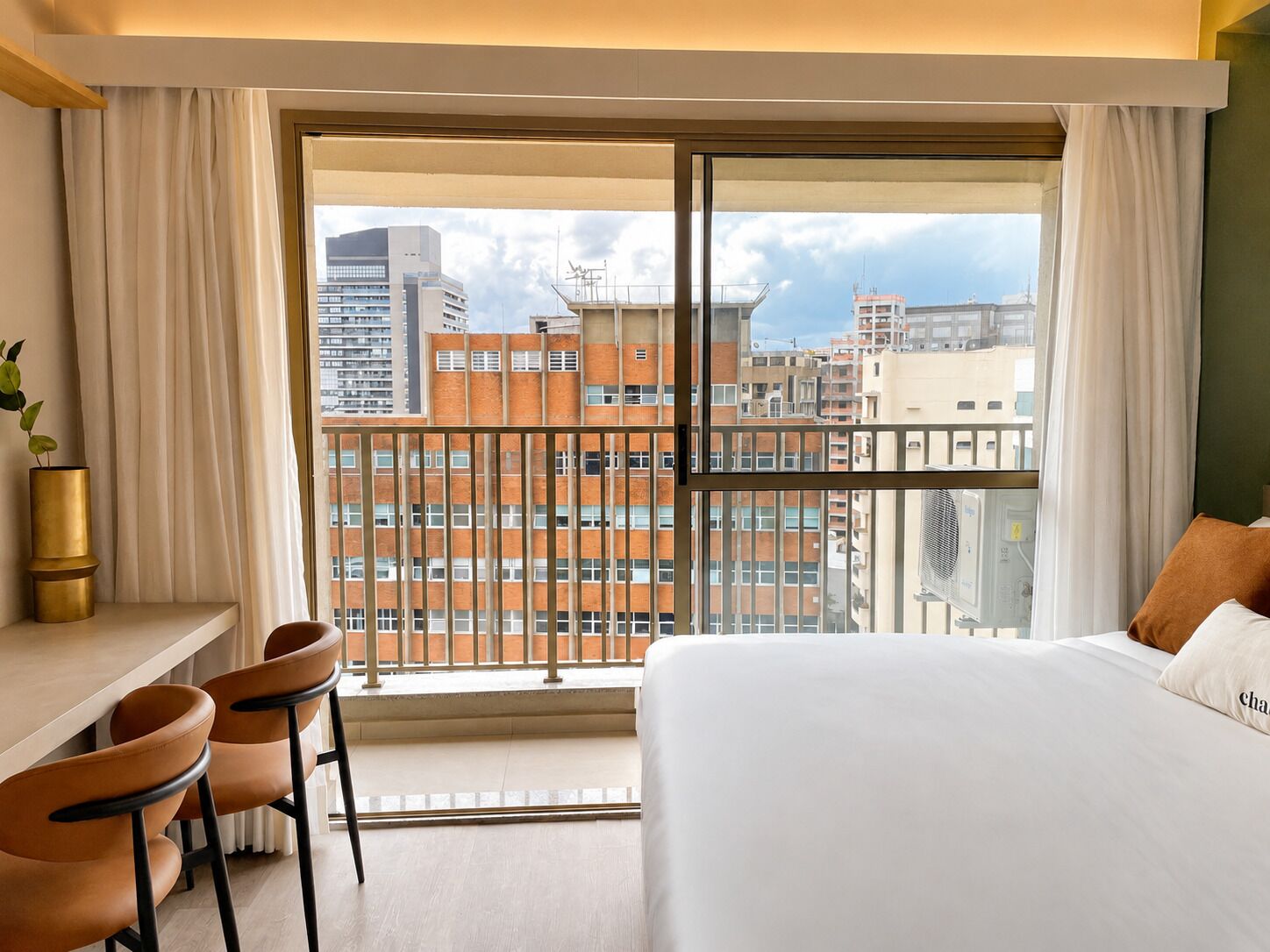 A hotel room with a large window, a bed, a desk, and chairs.