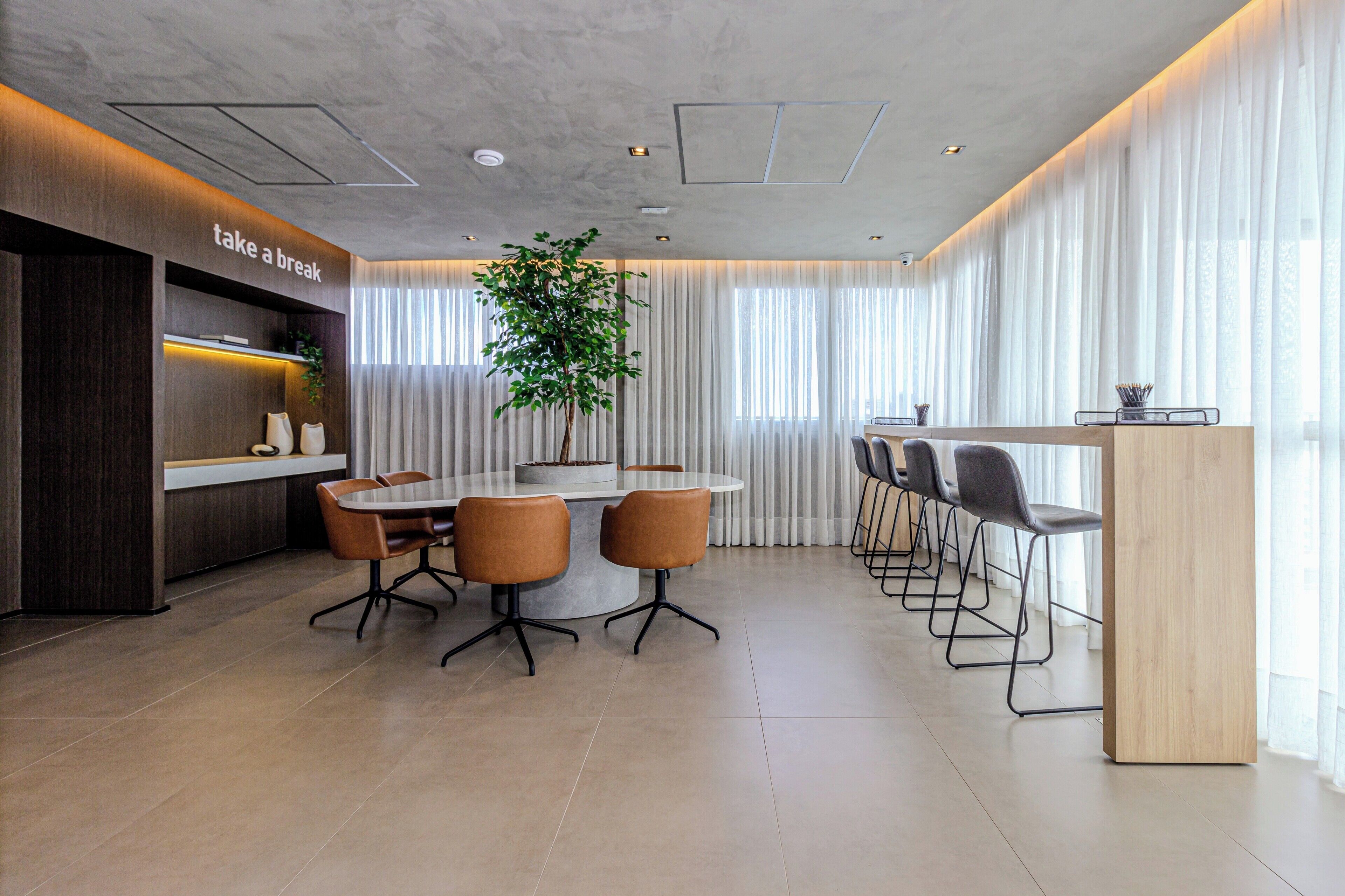 A modern conference room with a round table, brown chairs, a potted plant, and a 'take a break' sign.