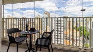 A balcony with a city view, two chairs, a table, and a bottle. - Charlie Nik Paradiso \ Soft Opening (São Paulo)