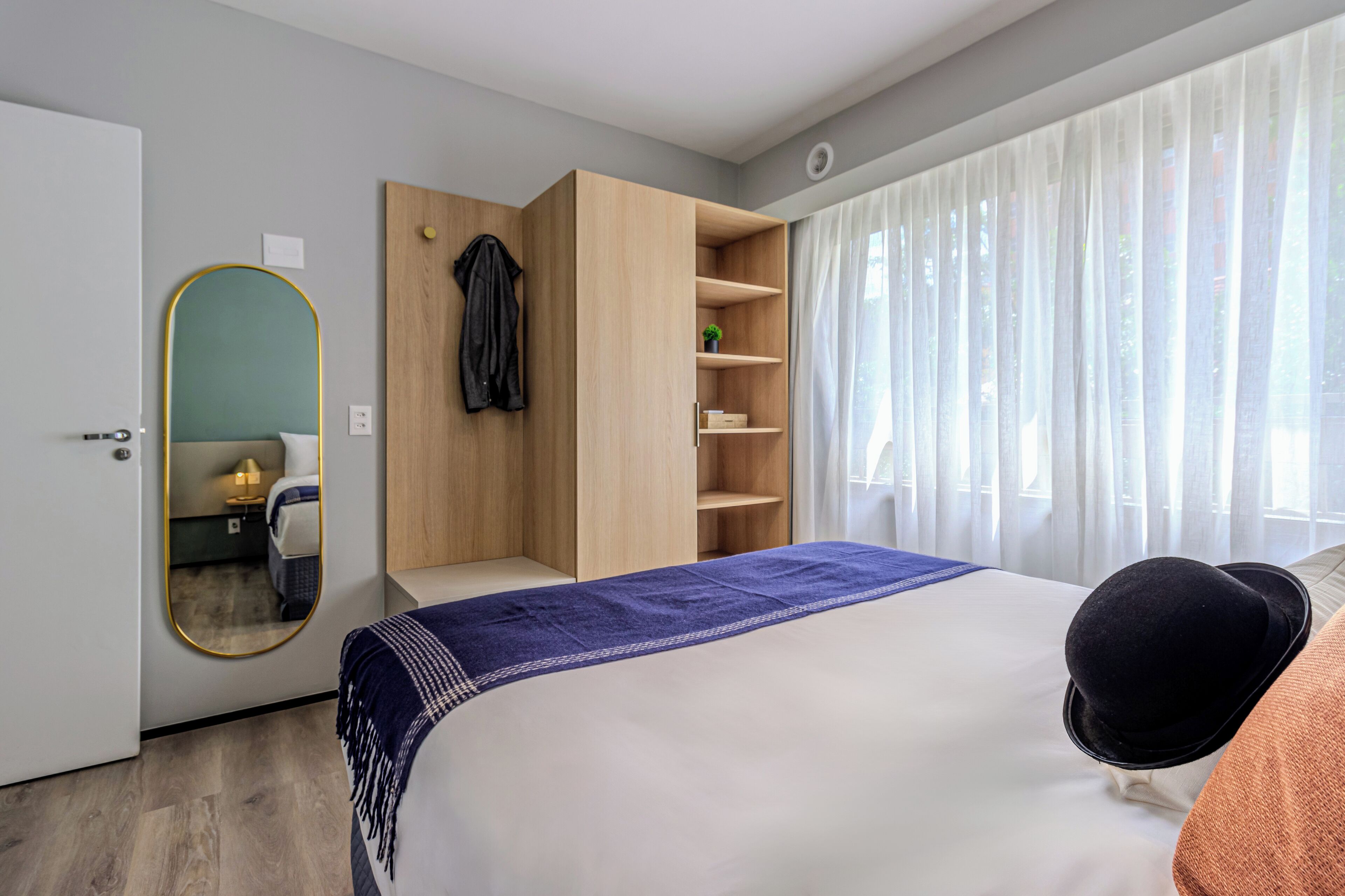 Una camera d'albergo moderna con un letto grande, un armadio, uno specchio e una finestra con tende.
