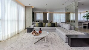 A modern living room with a grey sectional sofa, a round coffee table, and a large mirror. - Charlie Nik Paradiso \ Soft Opening (São Paulo)