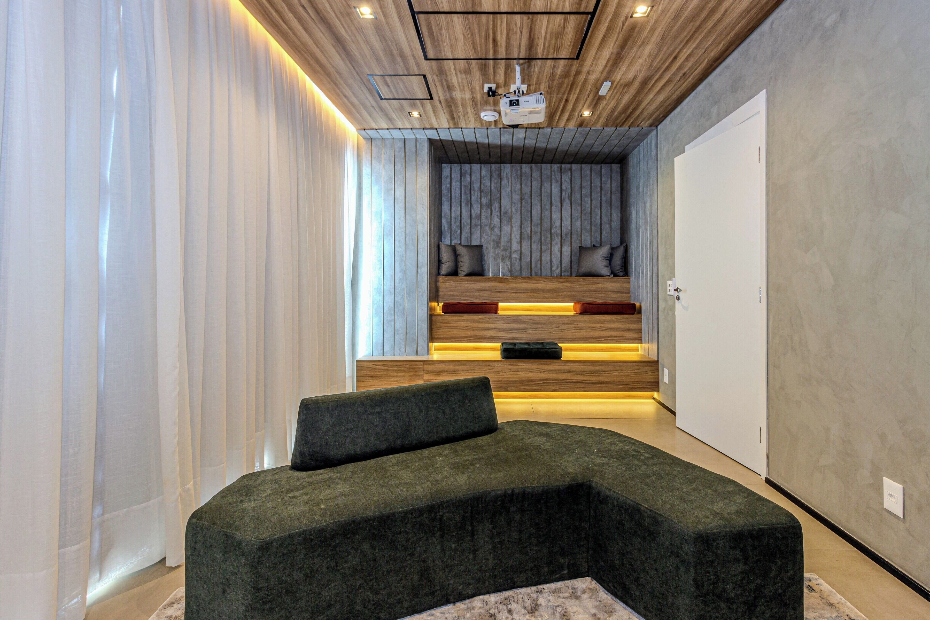 A modern bedroom with a curved green sofa, a built-in bench, and a ceiling projector.