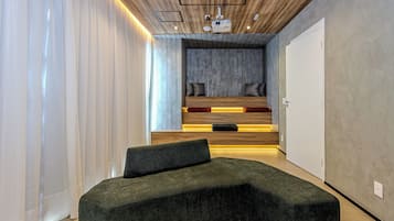A modern bedroom with a curved green sofa, a built-in bench, and a ceiling projector.