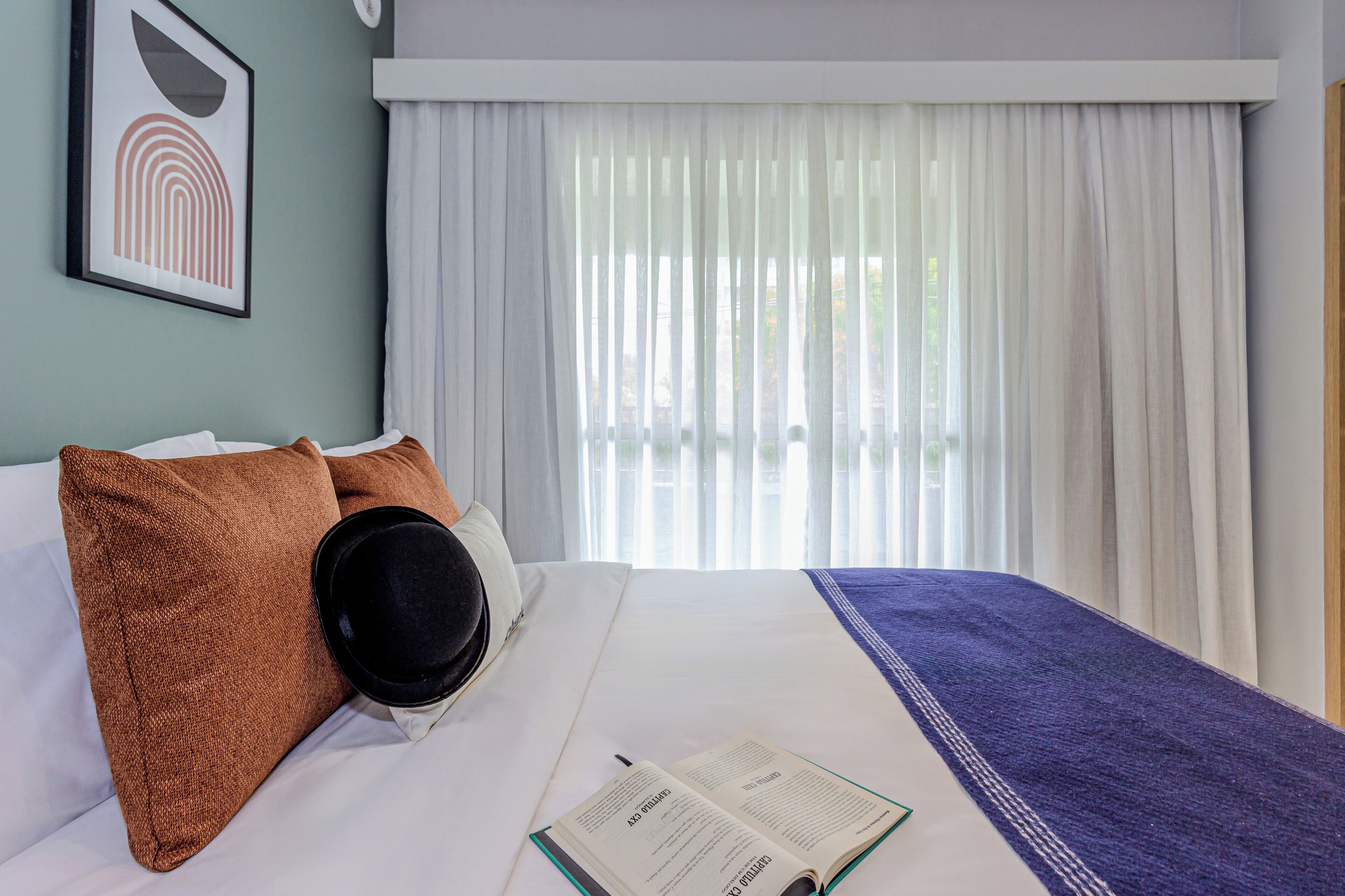 A neatly made bed with a book, a black hat, and two brown pillows.