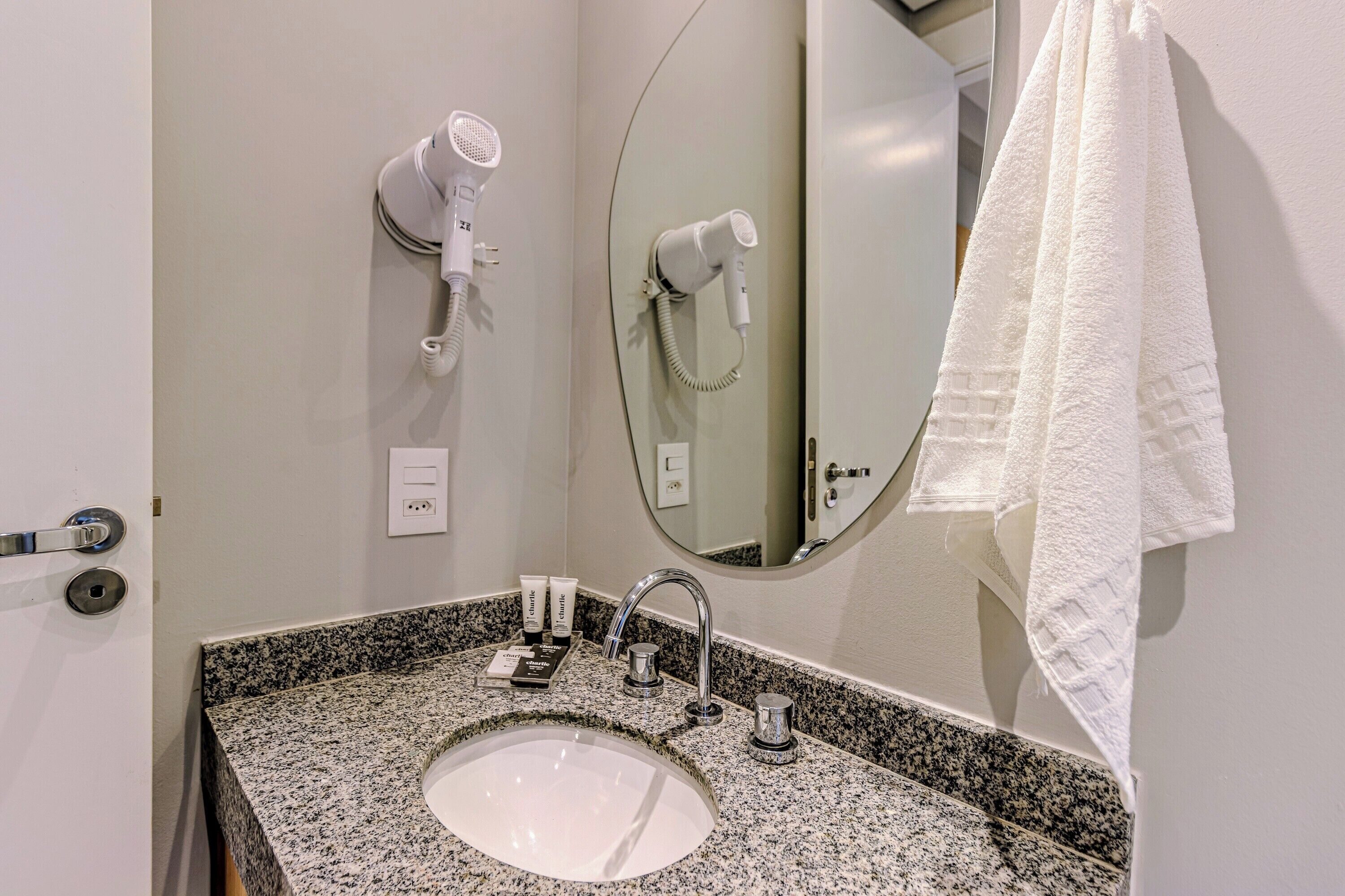 Bagno con lavabo su piano in granito, uno specchio, portasciùmani e un asciugacapelli fissato alla parete.