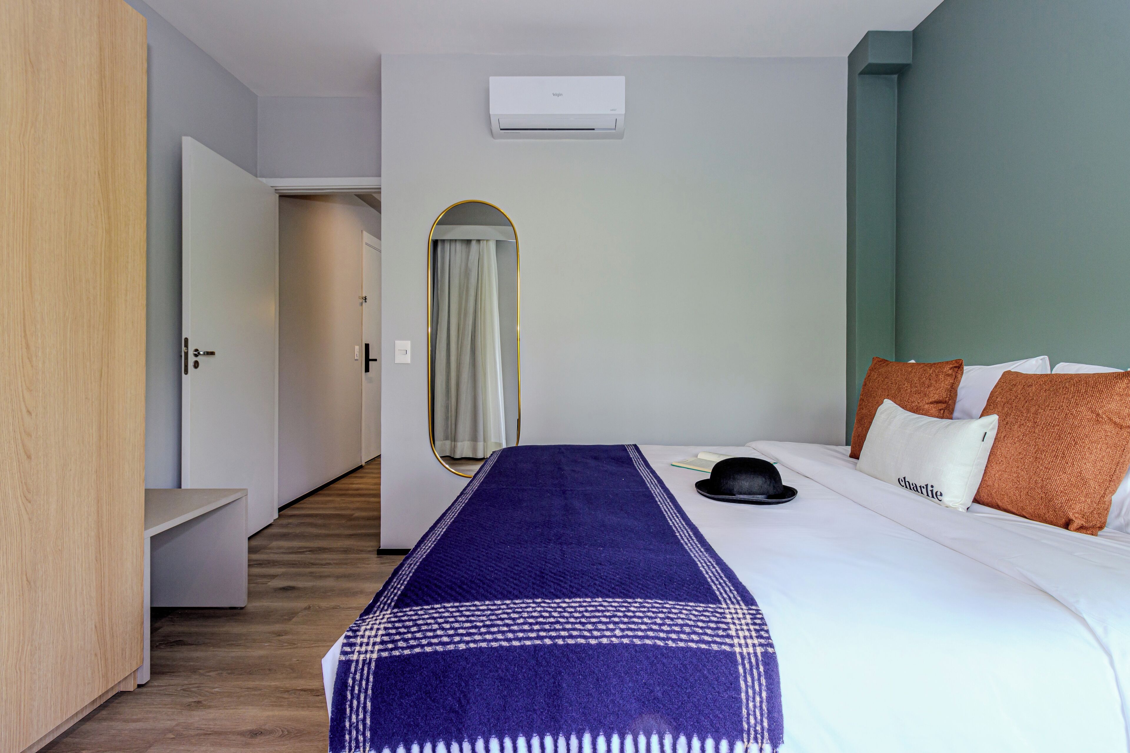 Une chambre d’hôtel avec un lit, une table de chevet, un miroir et un appareil de climatisation fixé au mur.