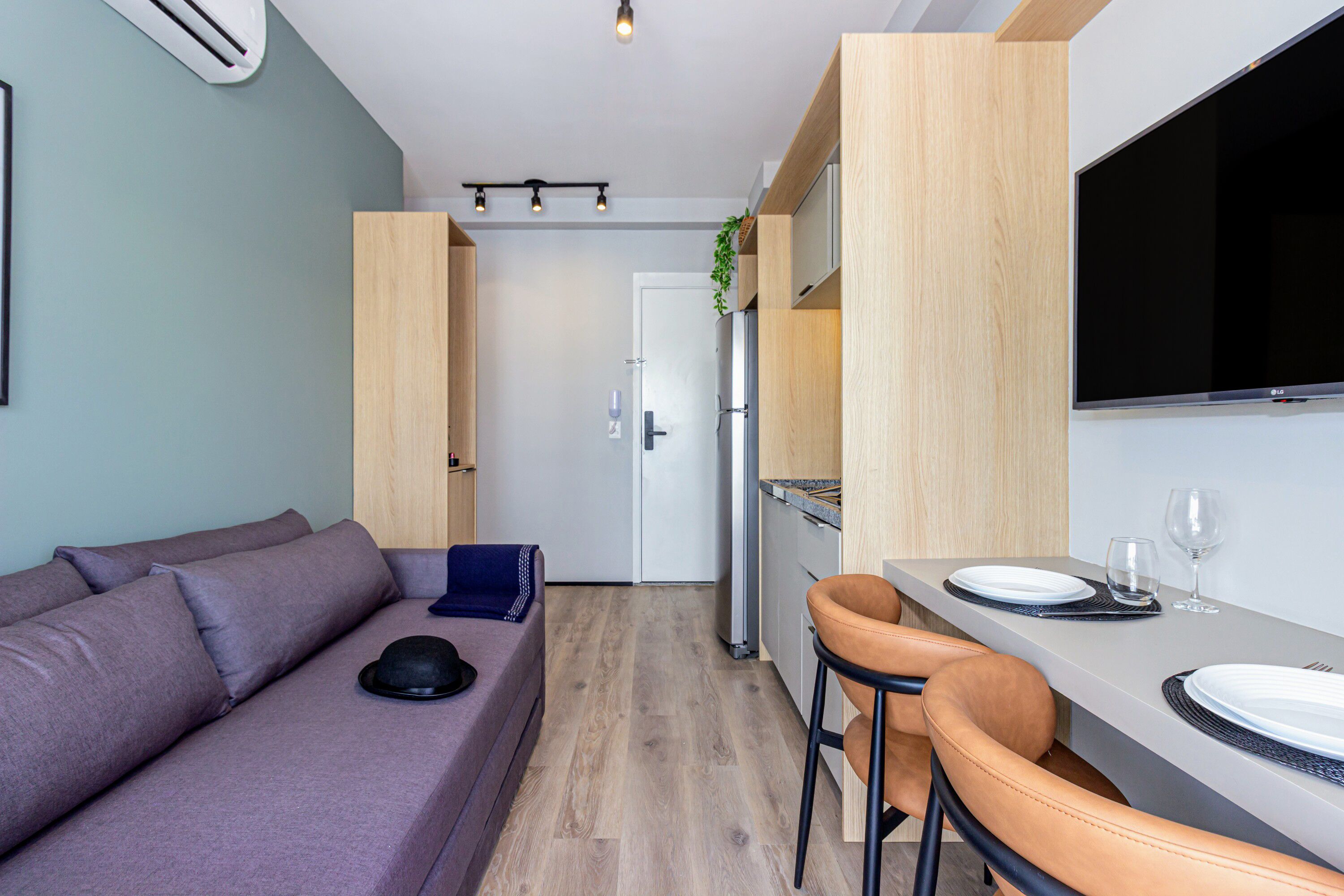 Ein kompakter Wohnraum mit einer Couch, einer Essecke mit Stühlen und einem Tisch sowie einer Küche mit Kühlschrank und Schränken.