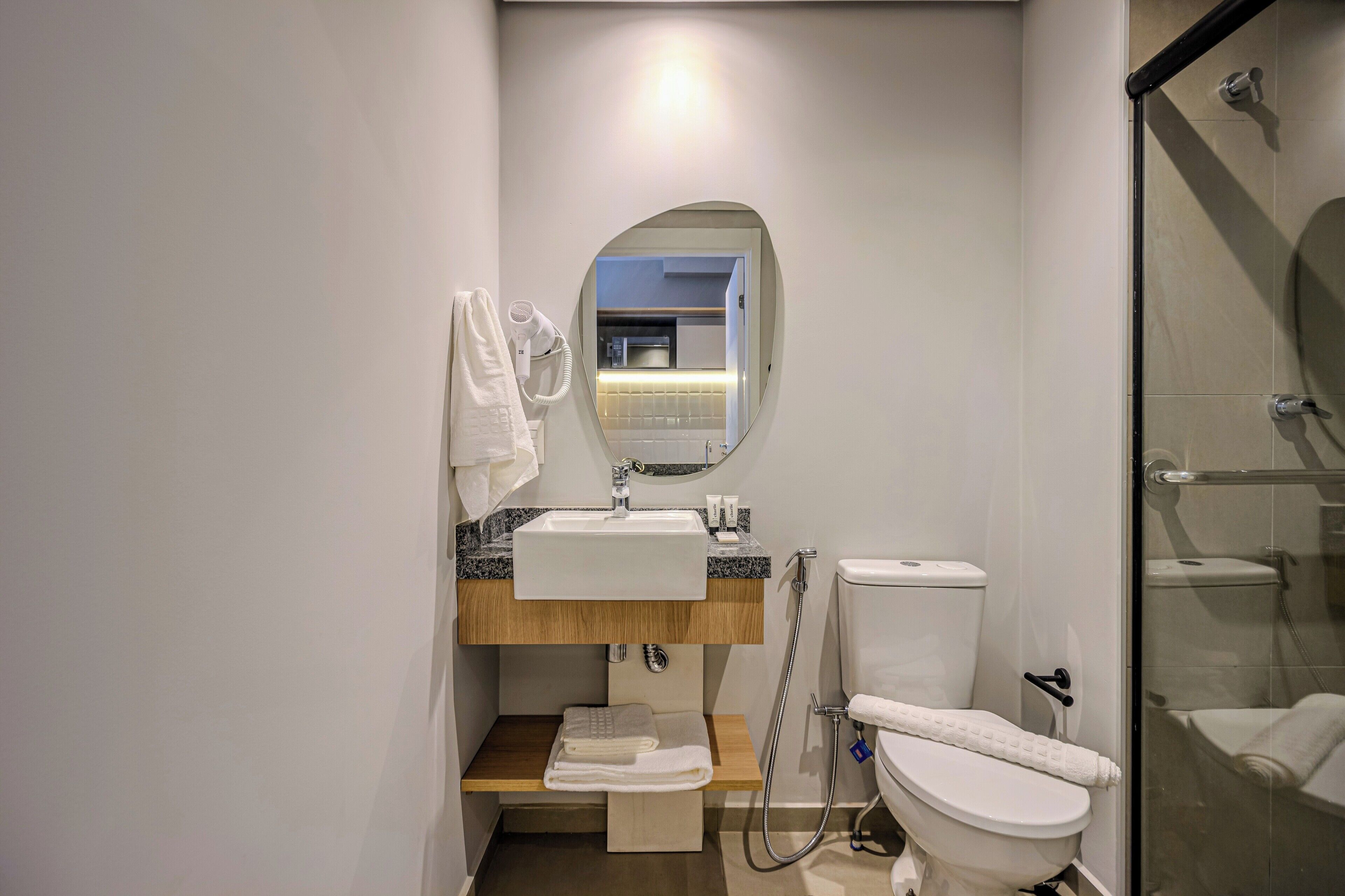 A modern bathroom with a white sink, mirror, and toilet. There is a towel rack and a shower area.