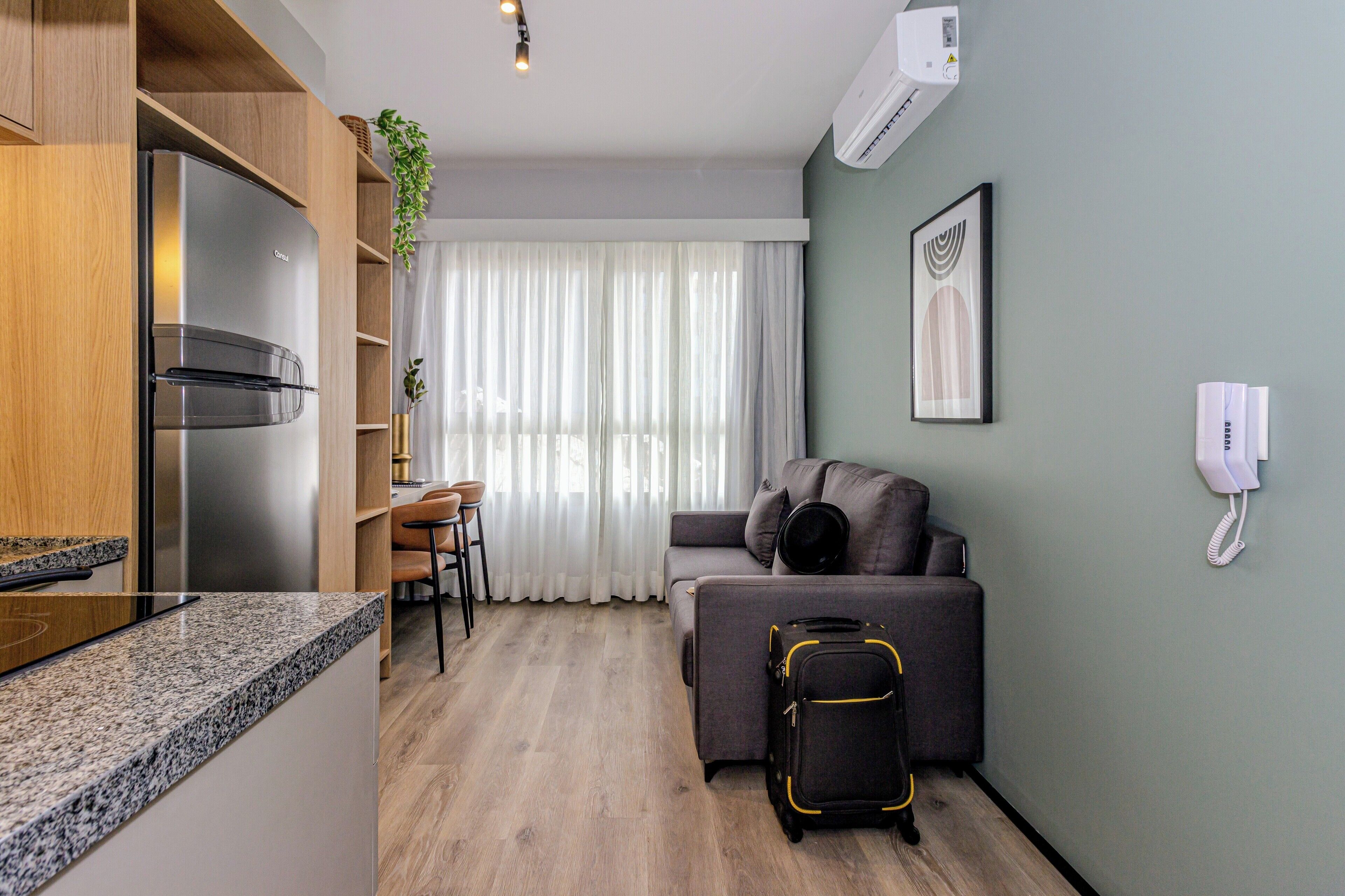 Eine moderne Küche mit integriertem Kühlschrank, ein Essbereich mit Tisch und Stühlen, ein graues Sofa und ein Koffer auf dem Boden.