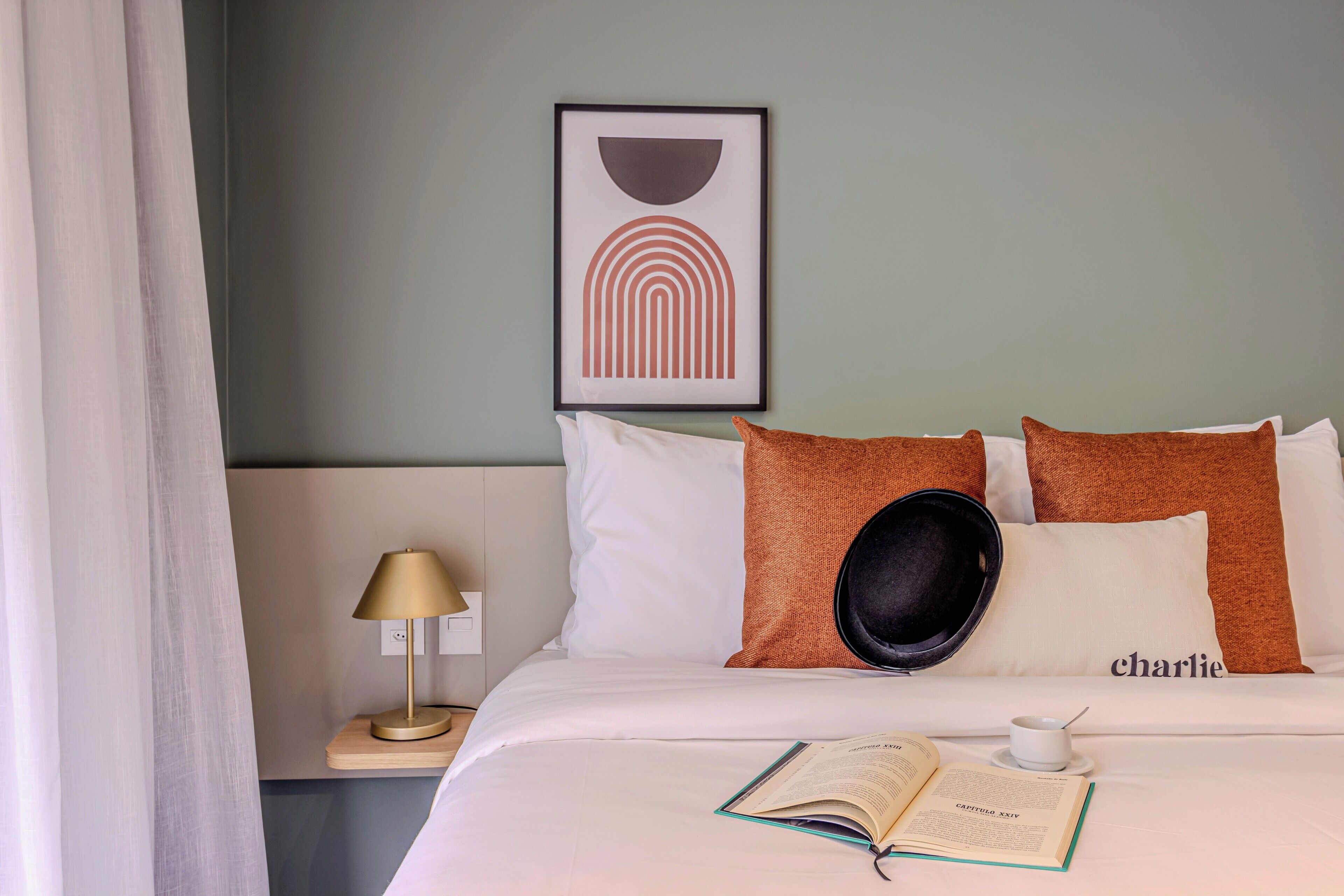 Un letto rifatto con cura, un libro e una tazza, un quadro appeso alla parete e una lampada sul comodino.