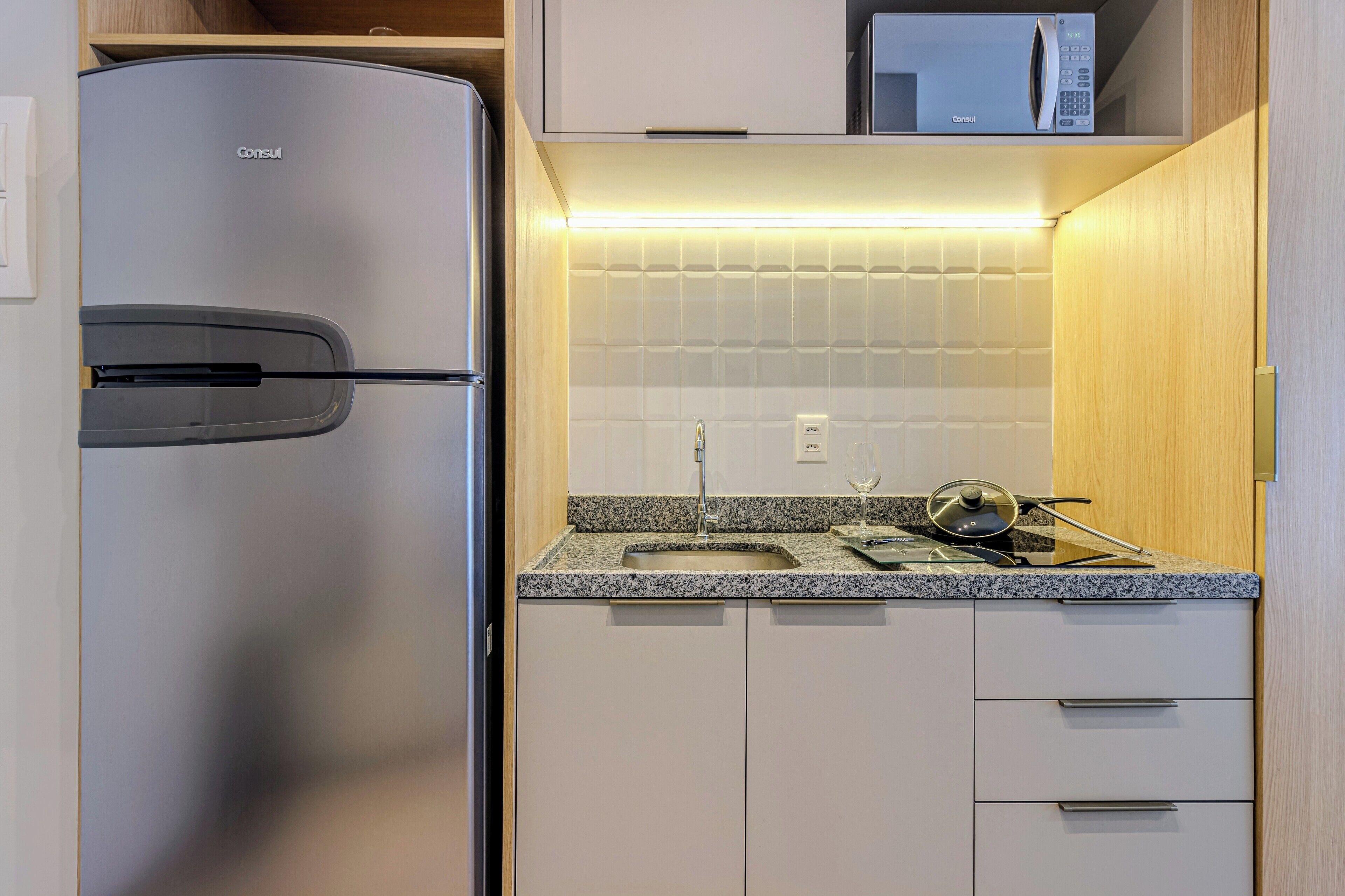 A modern kitchen with a stainless steel refrigerator, a microwave, a granite countertop, and a sink.