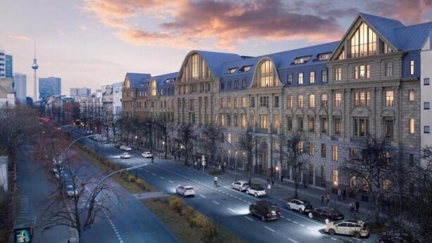 Un edificio grande e histórico de varias plantas con ventanas arqueadas, ubicado a lo largo de una calle con automóviles y peatones.