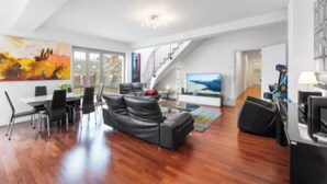 Amplia sala de estar con un sofá de cuero negro, una mesa de comedor con sillas y una escalera que conduce a un piso superior.