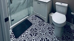 Moderni kylpyhuone, jossa on lasiseinäinen suihkukaappi, valkoinen pesuallas peilillä sekä wc-istuin.