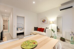 Ein modernes Wohnzimmer mit einem Holzesstisch, einer Couch mit roten und grauen Kissen, einer Stehlampe und einer Wandklimaanlage.