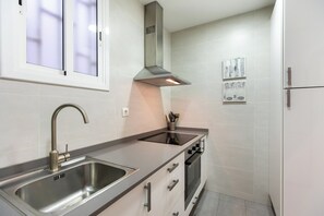 A modern kitchen with a stainless steel sink, a range hood, and a built-in oven. - Pere Serafí: Cozy apartment to experience the authentic Gràcia (Barcelona)