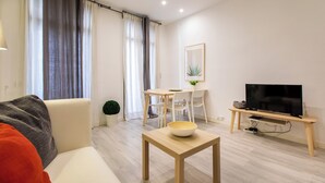 Ein modernes Wohnzimmer mit einer Couch, einem Esstisch mit Stühlen, einem Fernseher auf einem Schrank und einem kleinen Tisch mit einer Schüssel.
