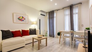 Ein modernes Wohnzimmer mit einem weißen Sofa, einem Holztisch und einem Essbereich inklusive Tisch und Stühlen.