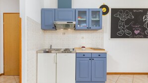 Uma cozinha compacta com armários azuis, um fogão e um quadro negro com desenhos.