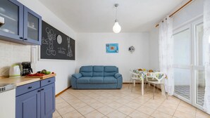 Un espace de vie compact comprenant un coin cuisine, un canapé bleu, une table à manger avec des chaises et une grande fenêtre.