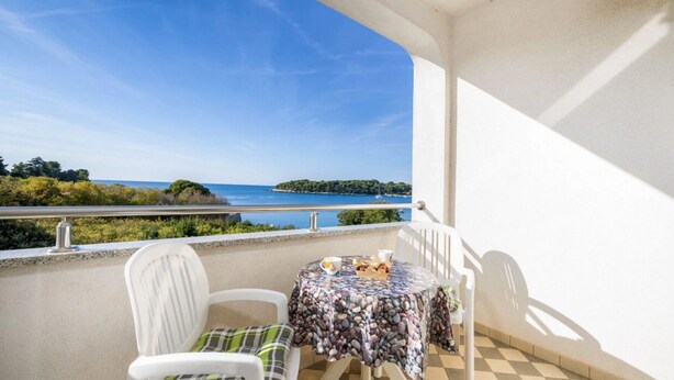 Un balcon avec une table et des chaises, offrant une vue sur la côte et un ciel dégagé.