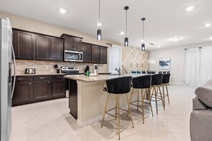 A modern kitchen with dark cabinets, a central island, bar stools, and pendant lighting. - 8BR house sleeps 20 with game room (Clermont)