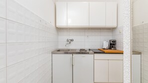 Eine kleine Küche mit weißen Schränken, einer Edelstahlspüle, einem Einbauherd und einer Kaffeemaschine auf der Arbeitsplatte.