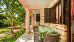 A covered outdoor dining area with a table set for two, stone walls, and wooden shutters. - Apartman Seaside 064 by Villas Guide (Pula)