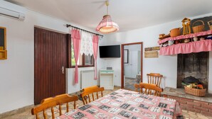 A dining area with a table covered in a checkered tablecloth, wooden chairs, a hanging light fixture, and a wall-mounted television. - Apartman Seaside 064 by Villas Guide (Pula)