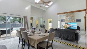 A spacious living area with a dining table set for four, a sofa, a television, and a stone wall with a clock. - Pleasant and RUSTIC 4-bedroom house in the heart of Orlando (Orlando)