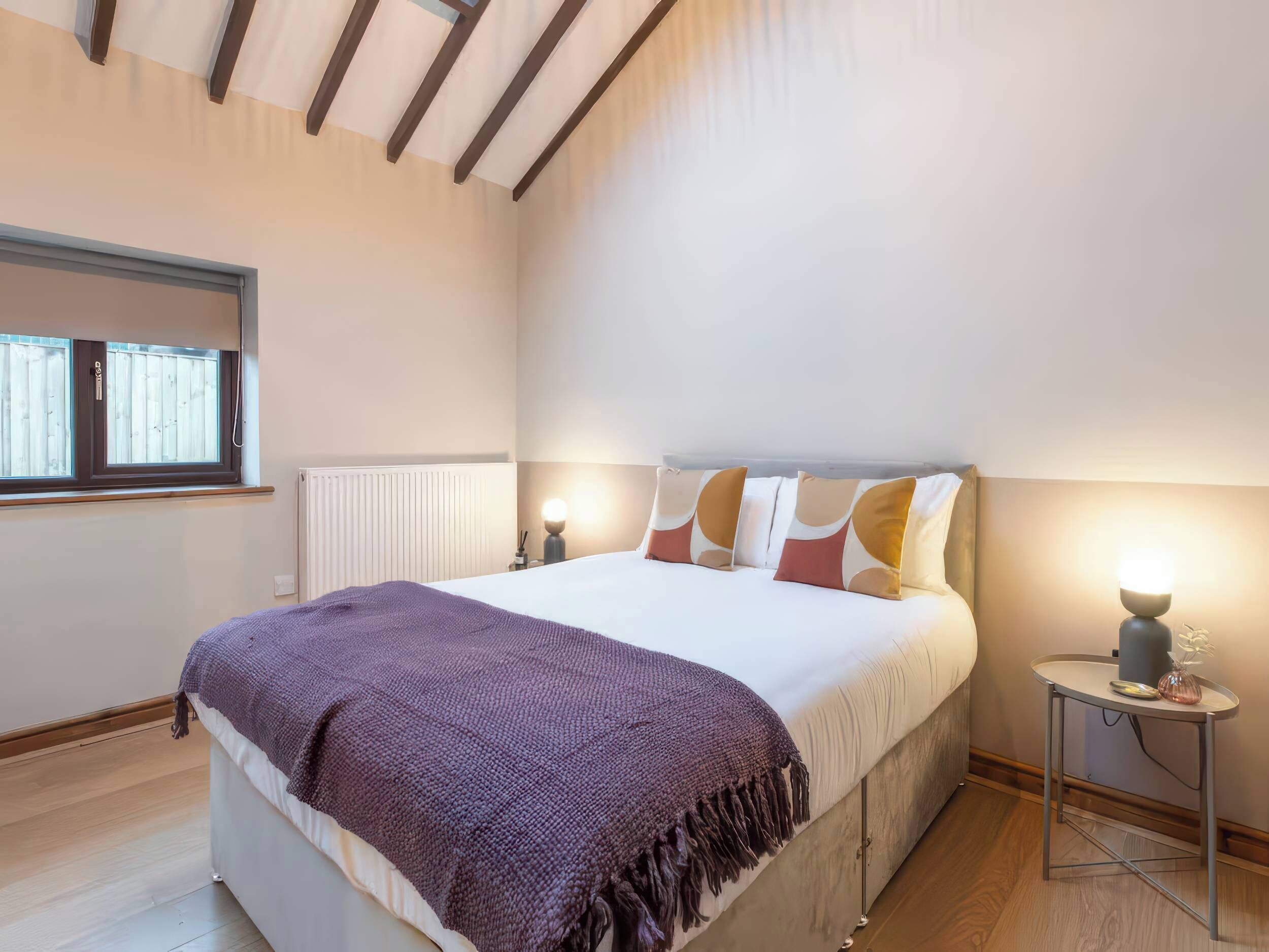 A bedroom with a bed, a window, a bedside table, and a lamp.