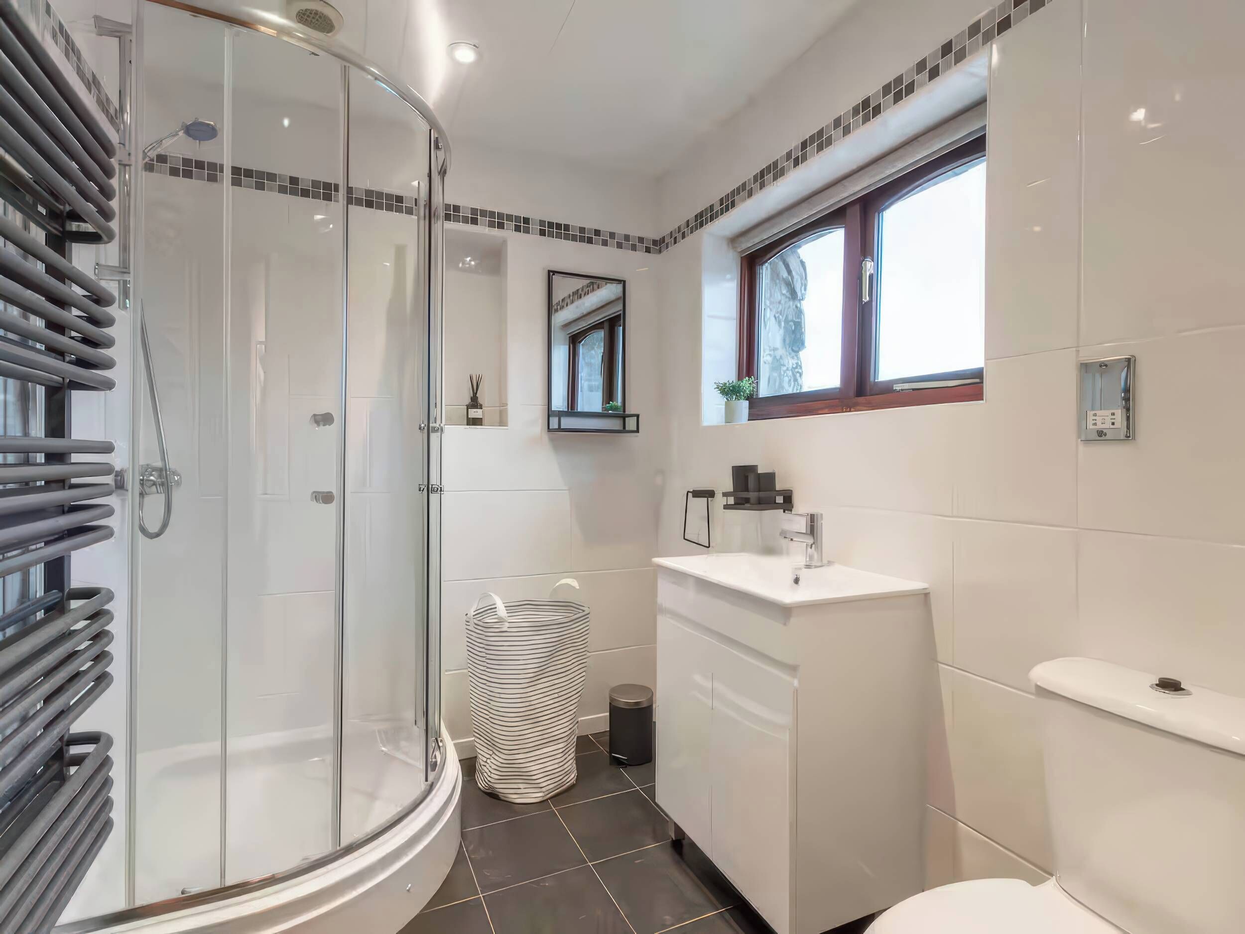 Un bagno moderno con doccia vetrata, lavandino bianco e specchio sopra, e una finestra che offre luce naturale.