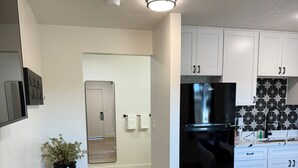 A modern kitchen with white cabinets, a black refrigerator, and a wooden floor. - CB&M Downtown Suites (Roosevelt)