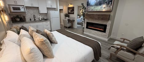 Un dormitorio moderno con una cama grande, chimenea, televisor y kitchenette.