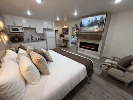 Quarto moderno com uma cama grande, lareira, televisão e cozinha compacta.