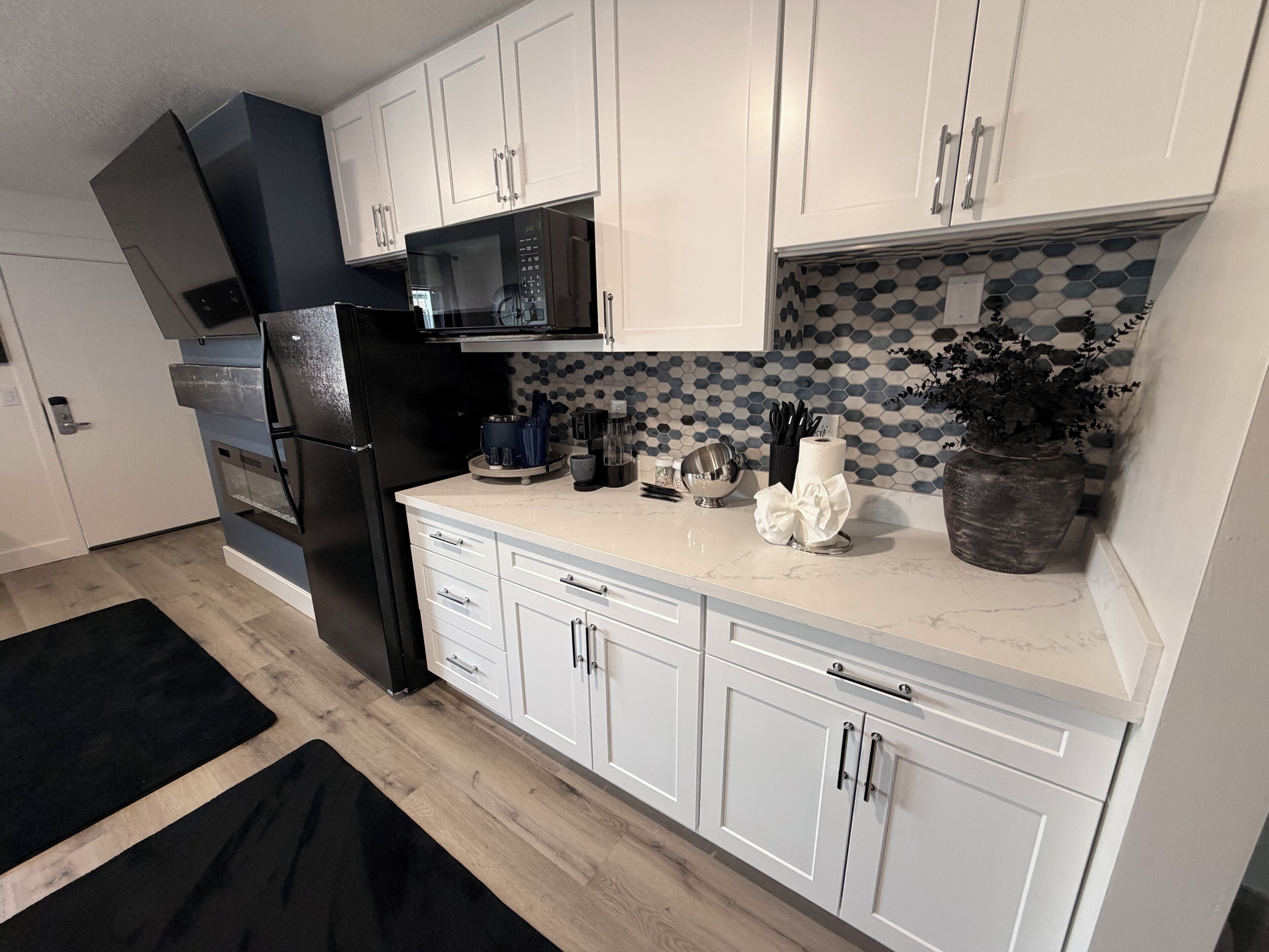 A modern kitchen with white cabinets, a black refrigerator, a microwave, and a coffee maker.