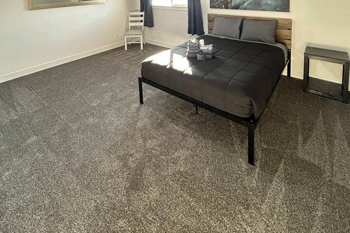 Une chambre à coucher avec un lit, une chaise, une petite table, un tableau et une fenêtre avec des rideaux.
