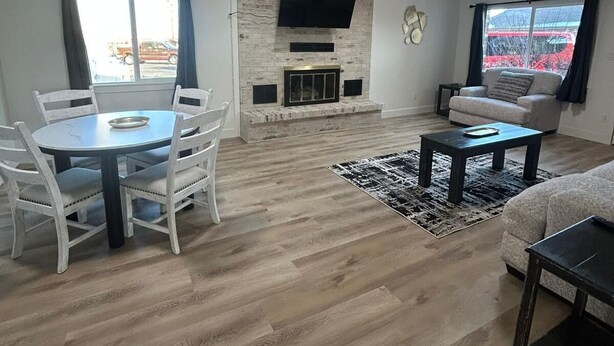 A modern living room with a fireplace, a flat-screen TV mounted on the wall, a dining area with a round table and white chairs, and a sofa in a corner. - CB&M Downtown Suites (Roosevelt)