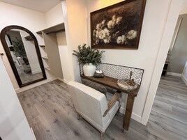 Um corredor com espelho, um banco, uma planta em vaso, um quadro e uma parede com padrão herringbone.