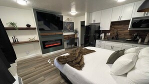 A modern bedroom with a large bed, a fireplace, and a kitchen area. - CB&M Downtown Suites (Roosevelt)